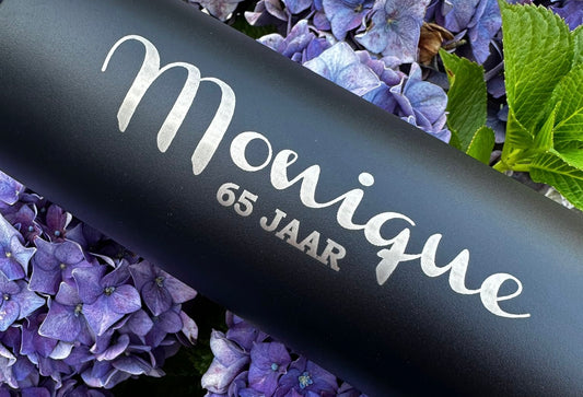 Zwarte drinkfles met daarop Monique 65 jaar gegraveerd op een achtergrond van blauwe bloemen