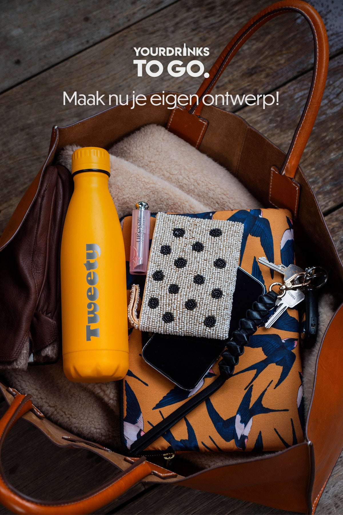 Gele thermosfles met tweety gravure in een gevulde bruine tas op een houten vloer